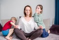 Mom sits on the sofa meditating lotus position, little children scream playing around focused calm mom meditating balancing while