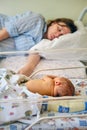 Mom is sleeping in the ward with a newborn baby, a maternity hospital bracelet on her arm. A newly born child in a clinic crib Royalty Free Stock Photo