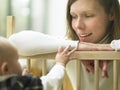 Mom Smiling at Baby Over Playpen Railing