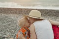 Mom and son embrace on a pebble beach. Sunset time. Back view Royalty Free Stock Photo