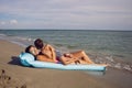 mom and son are lying on the beach on inflatable blue mattress during the summer vacation