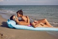 mom and son are lying on the beach on inflatable blue mattress during the summer vacation