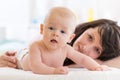 Mom and son lying down on bed in nursery room. Mother embracing infant baby. Kid looking at camera. Royalty Free Stock Photo