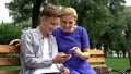 Mom and son reading funny stories on smartphone, sitting on bench in park, fun
