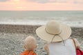 Mom and son rest on the pebble beach. Sunset time. Back view Royalty Free Stock Photo