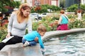 Mom and son sit at the fountain in the city center and enjoy the freshness of the water in the hot summer