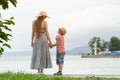 Mom and son standing on the pier and look at each other on the sea background, lighthouse and mountains in the distance.