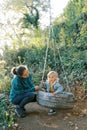 Mom is squatting next to a little girl sitting on a tire swing in the park Royalty Free Stock Photo