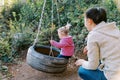 Mom swings a little girl on a tire swing in the forest. Back view Royalty Free Stock Photo