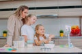 Mom teaches her daughters to cook dough in the kitchen. The family is filming a culinary video on a smartphone