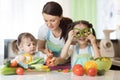 Mom teaches two daughters to cook at the kitchen table with raw food