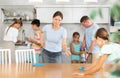 Mom tells daughter to wipe kitchen table thoroughly, family do kitchen chores in background