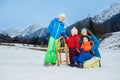 Mom and three children play outside on snow slope with sledge