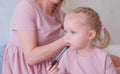 Mom tie hair into braids to her little charming daughter in pink dresses while she keep felt-pen. Royalty Free Stock Photo