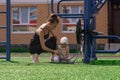 Mom and toddler daughter are walking on the sports ground near the house, the baby is interested in a exercise machine