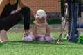 Mom and toddler daughter are walking on the sports ground near the house, the baby is interested in a exercise machine