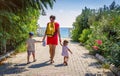 Mom and two children hold hands and walk along the path to the sea on clear, sunny summer day on vacation