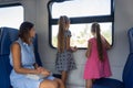 Mom and two daughters ride in an electric train, children standing looking out the window