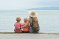 Mom and two sons sit on the pier and admire the sea and the mountains in the distance. Back view Royalty Free Stock Photo