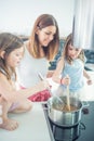 Mom with two young twins daughters in the kitchen cooking spaghetti