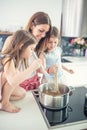 Mom with two young twins daughters in the kitchen cooking spaghetti