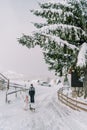 Mom watches a little girl walking along a snowy village road behind a tabby cat Royalty Free Stock Photo