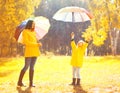 Moment of happiness! Happy family with umbrellas in sunny autumn rainy day, young mother and child in jacket outdoors