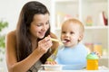 Mommy giving healthy food to baby son on high chair in kitchen. Royalty Free Stock Photo