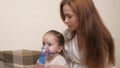 Mommy inhales a little girl in a mask with a nebulizer at home. The child is receiving respiratory therapy with a Royalty Free Stock Photo