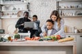 Mommy teaching lovely kid to cook while father and child boy spending time using laptop computer Royalty Free Stock Photo