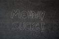 Monday sucks written in chalk on a blackboard. Handwritten