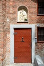 Ancient wooden door with nails and Virgin Mary bas relief in a sunny day in Mondovi, Italy