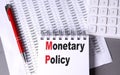 MONETARY POLICY text on notebook with pen, calculator and chart on grey background