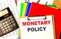 MONETARY POLICY text written on paper clipboard with chart and calculator