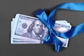 Money as gift concept, win or bonus, hundred dollar bills on grey background. Pile of 100 dollar bills is tied with blue ribbon Royalty Free Stock Photo