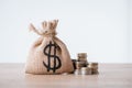 Money bag with dollar sign and stacks of metal coins on wooden surface