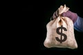 Money bag with US dollar sign. Man hand with money bag on black background with copy space. Bank robber.