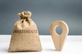 Money bag with the word Investments and a geolocation marker. Point and direct investments in a region or country. Construction of