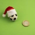 Money, christmas and football. A soccer ball in a red Santa Claus hat next to a one euro coin on a green background. Square frame Royalty Free Stock Photo