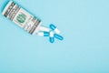 Money dollar rolled up with pills flowing out isolated on blue background, high costs of expensive medication concept. Copy space