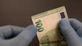 Money exchange during Covid-19 times: Hands with blue protective medical gloves are counting European 100 hundred EURO