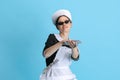 Bossy young woman in chambermaid uniform and stylish sunglasses isolated over blue background