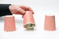 Money fraud. Close up of male hand opens paper cup, showing rolled-up dollars. White background. Concept of scamming