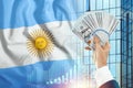 Money in a man`s hand against the background of the flag of Argentina. The financial condition of the inhabitants of Argentina,