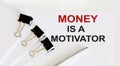 MONEY IS A MOTIVATOR written on a white page with office tools