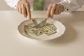 Money on a plate being cut like food with a knife and fork