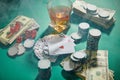 Money, playing cards, dice and casino tokens near glass of cognac with smoke around on green