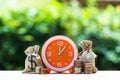 Money bags and orange clock on wooden table with nature backgro Royalty Free Stock Photo