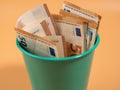 Money in the trash can on an orange background. Euros in the trash. Waste of money concept. Royalty Free Stock Photo