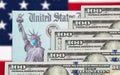 Money and United States IRS Stimulus Check with Statue of Liberty Wearing Face Mask Resting on American Flag Royalty Free Stock Photo